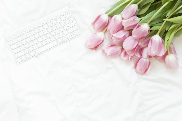 Flat lay of a white wireless keyboard and a bunch of pink tulips on a white fabric background