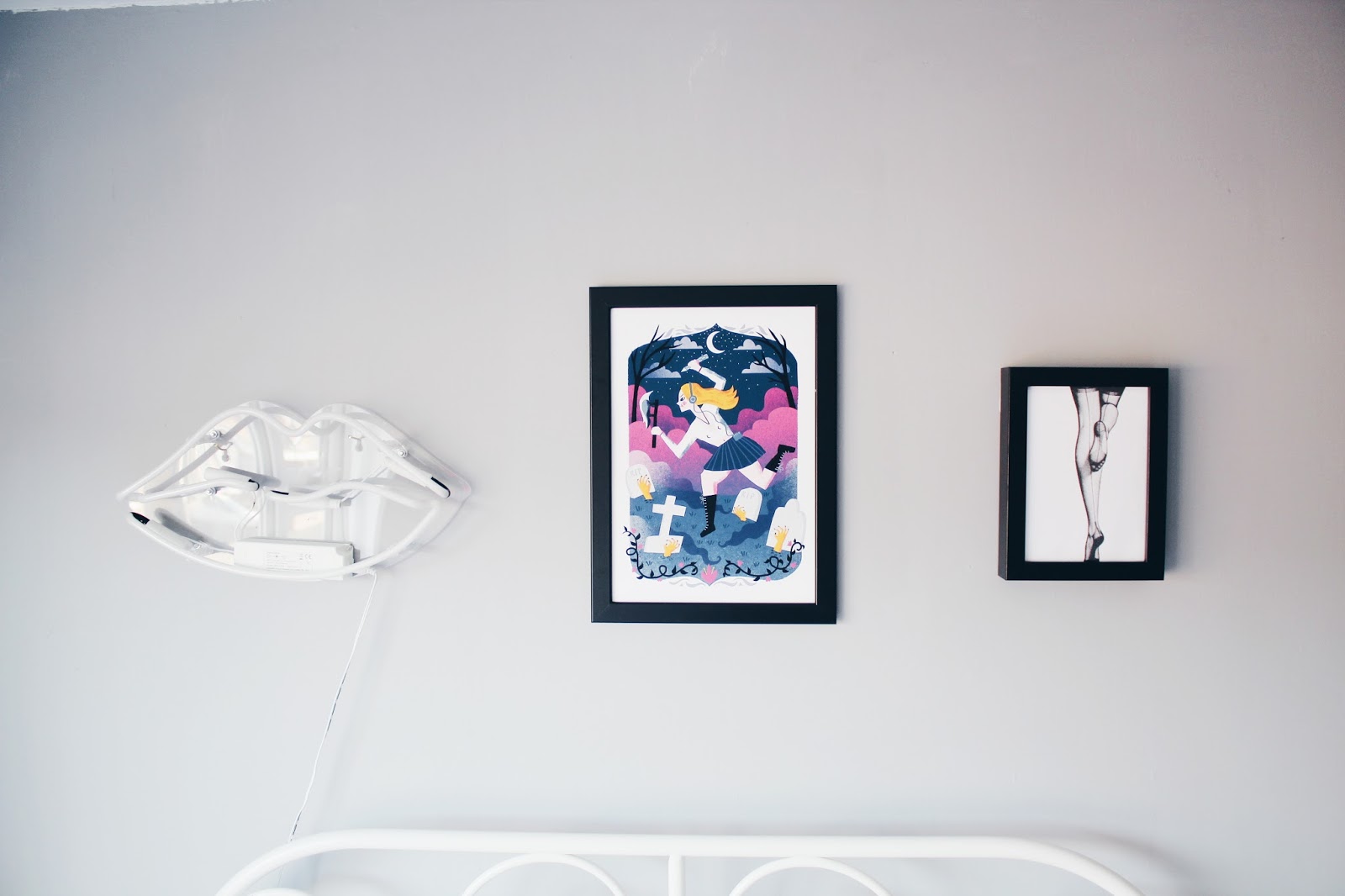 Grey wall decorated with a lip-shaped light fixture and two framed illustrations, one colorful and one black and white