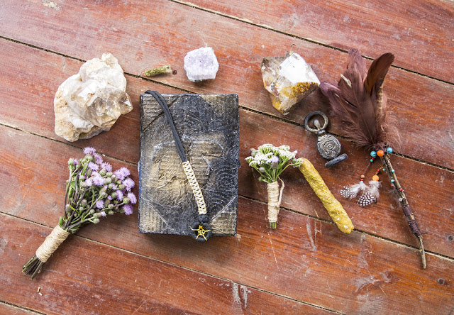 Assorted natural items including crystals, stones, a feather, dried flowers tied with twine, and a dark covered book