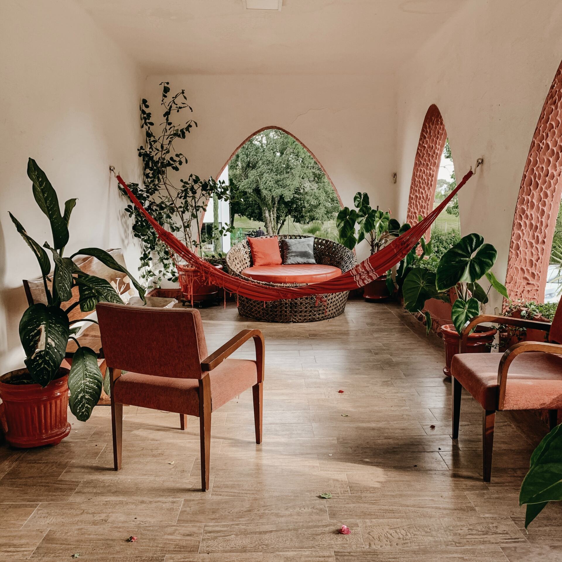 Covered patio with arched terracotta doorways, a red hammock, round woven daybed, orange chairs, and potted plants